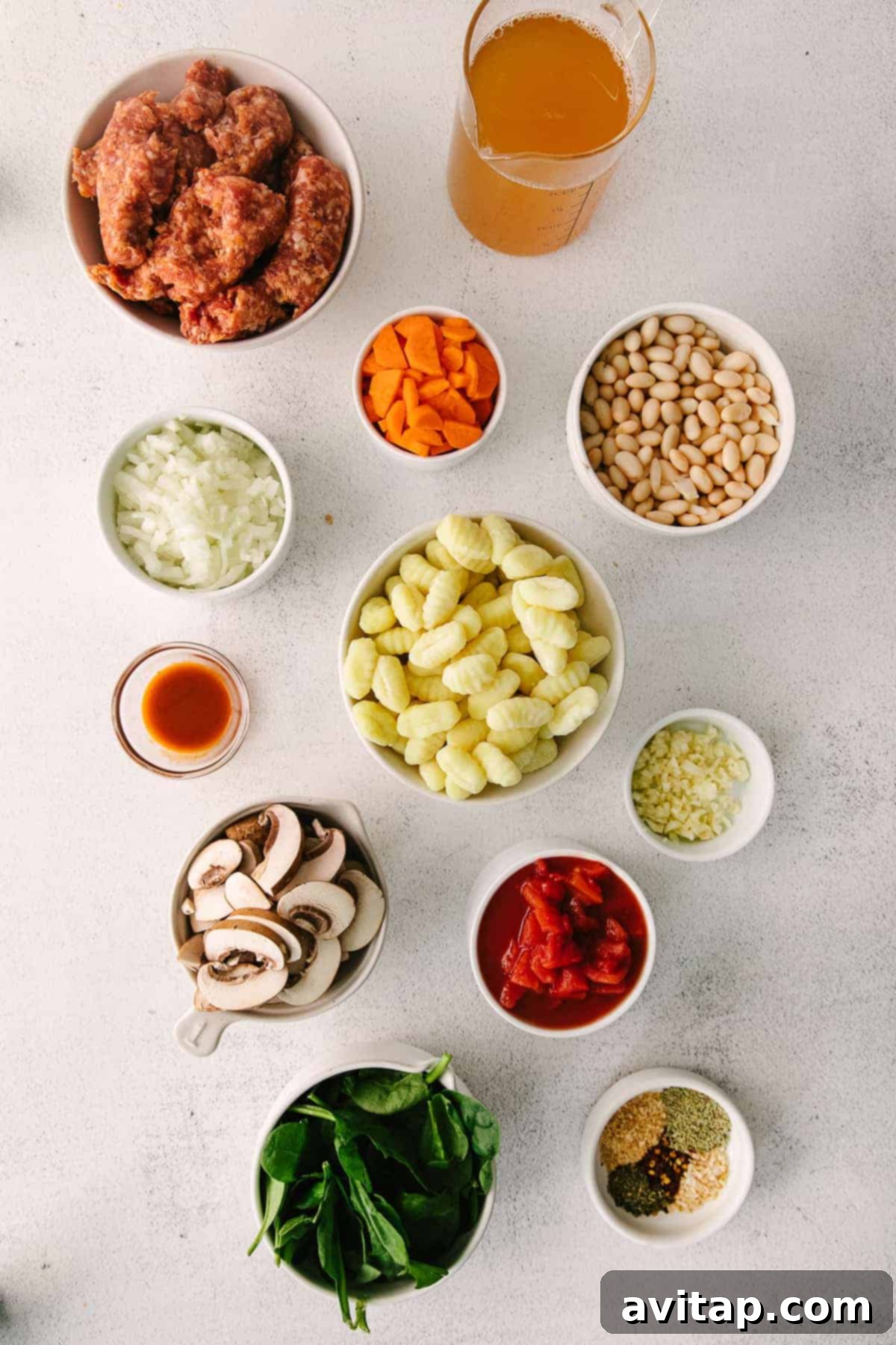 A vibrant selection of fresh ingredients including Italian sausage, sliced mushrooms, carrots, spinach leaves, and potato gnocchi, arranged in small bowls, ready for cooking this delicious one-pot soup.