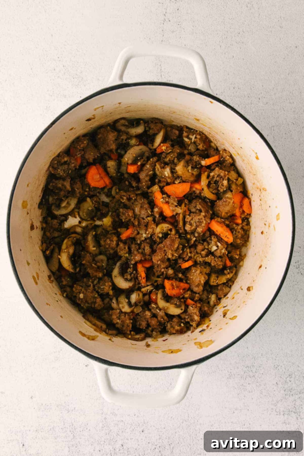 Sausage gnocchi soup simmering in a large stock pot on the stove, with vibrant vegetables and broth creating a rich aroma.