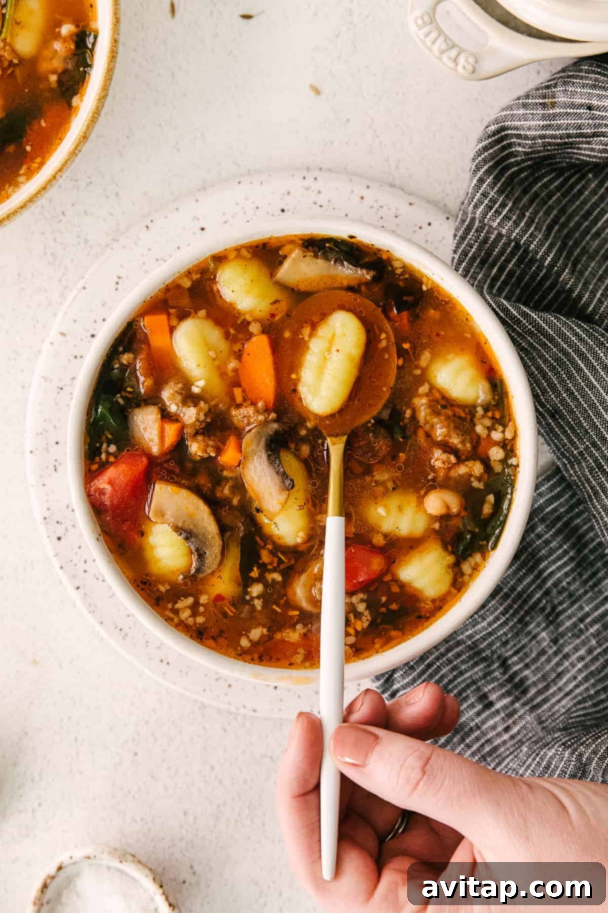 A close-up shot of a single tender potato gnocchi being lifted from a bowl of hearty sausage gnocchi soup with a spoon, highlighting its perfectly cooked, pillowy texture.
