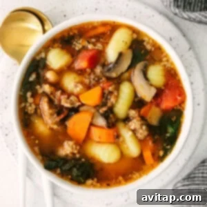 A warm bowl of homemade sausage gnocchi soup, garnished with fresh parsley and a sprinkle of cheese.