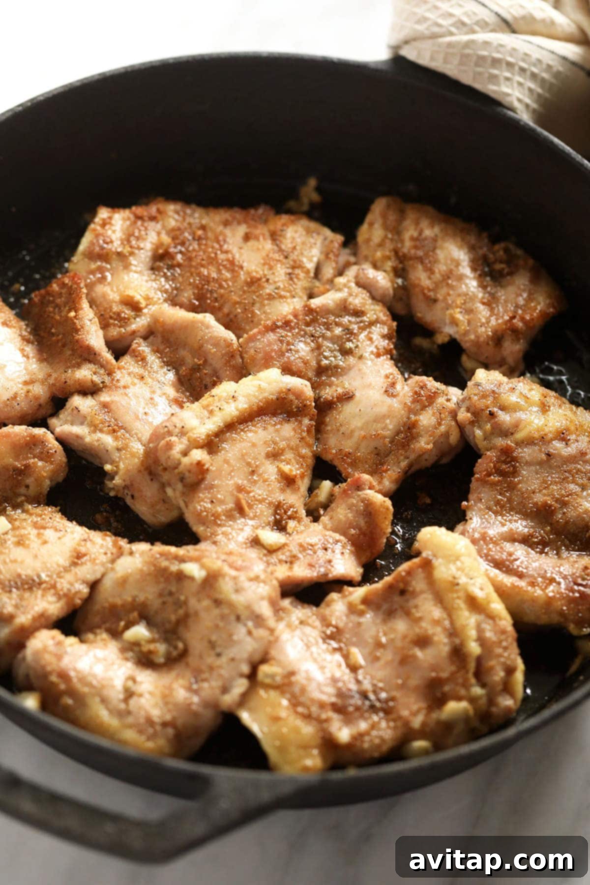 Boneless chicken thighs seasoned with a fragrant dry rub in a cast iron skillet, ready for searing to create a savory crust