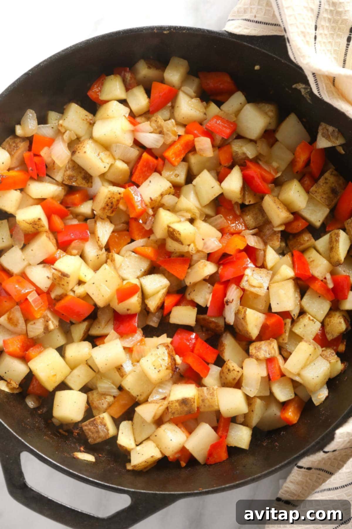 Diced russet potatoes and vibrant red bell peppers mingling in a cast iron skillet, lightly sautéed