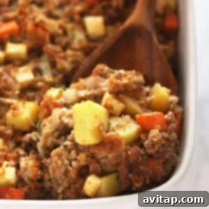 Sausage stuffing in a white baking dish with a wood spoon.