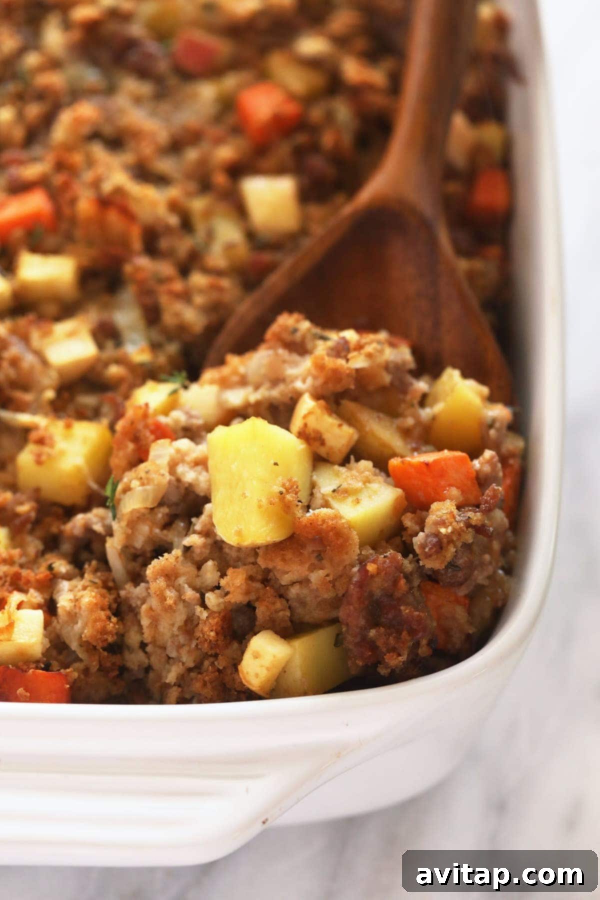 A wooden spoon lifting a generous scoop of hot, savory sausage stuffing, ready to be placed on a plate.