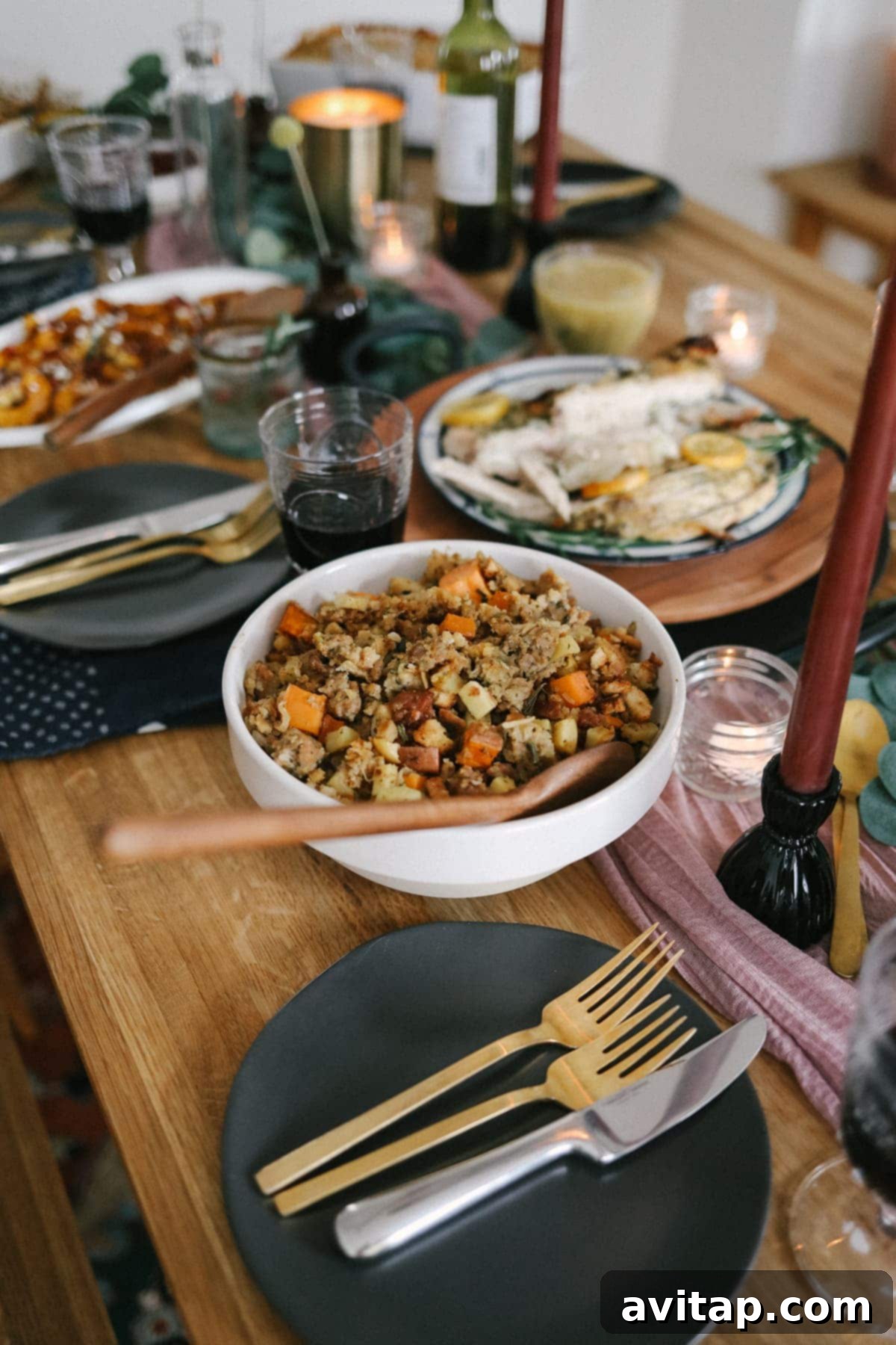 A close-up of baked sausage stuffing in a white ceramic bowl, showcasing its golden crust and herbaceous texture.