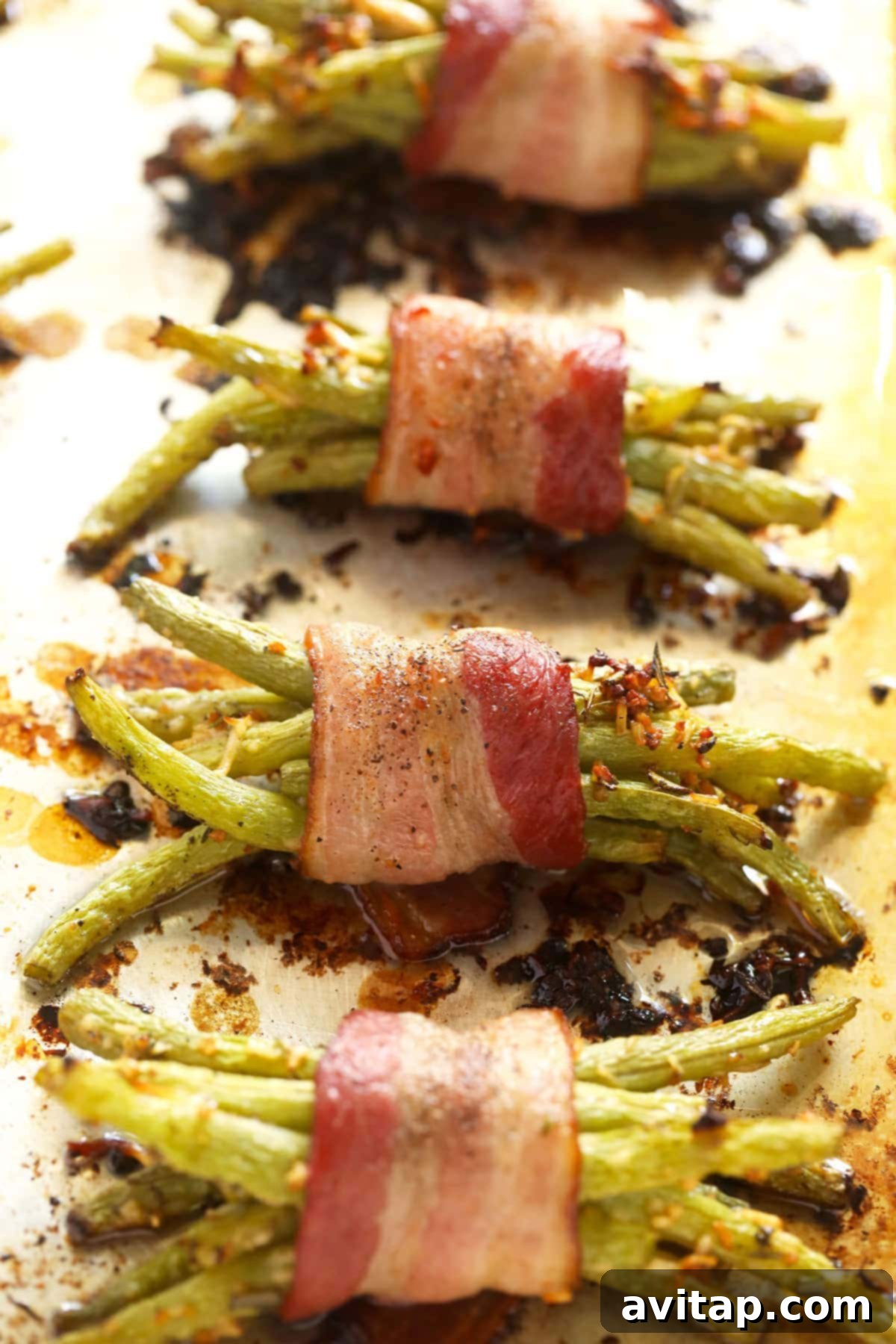 Baked bacon wrapped green beans cooling on a baking sheet, freshly out of the oven