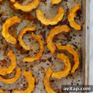 Roasted delicata squash glistening on a baking sheet, fresh from the oven, showing golden-brown edges.