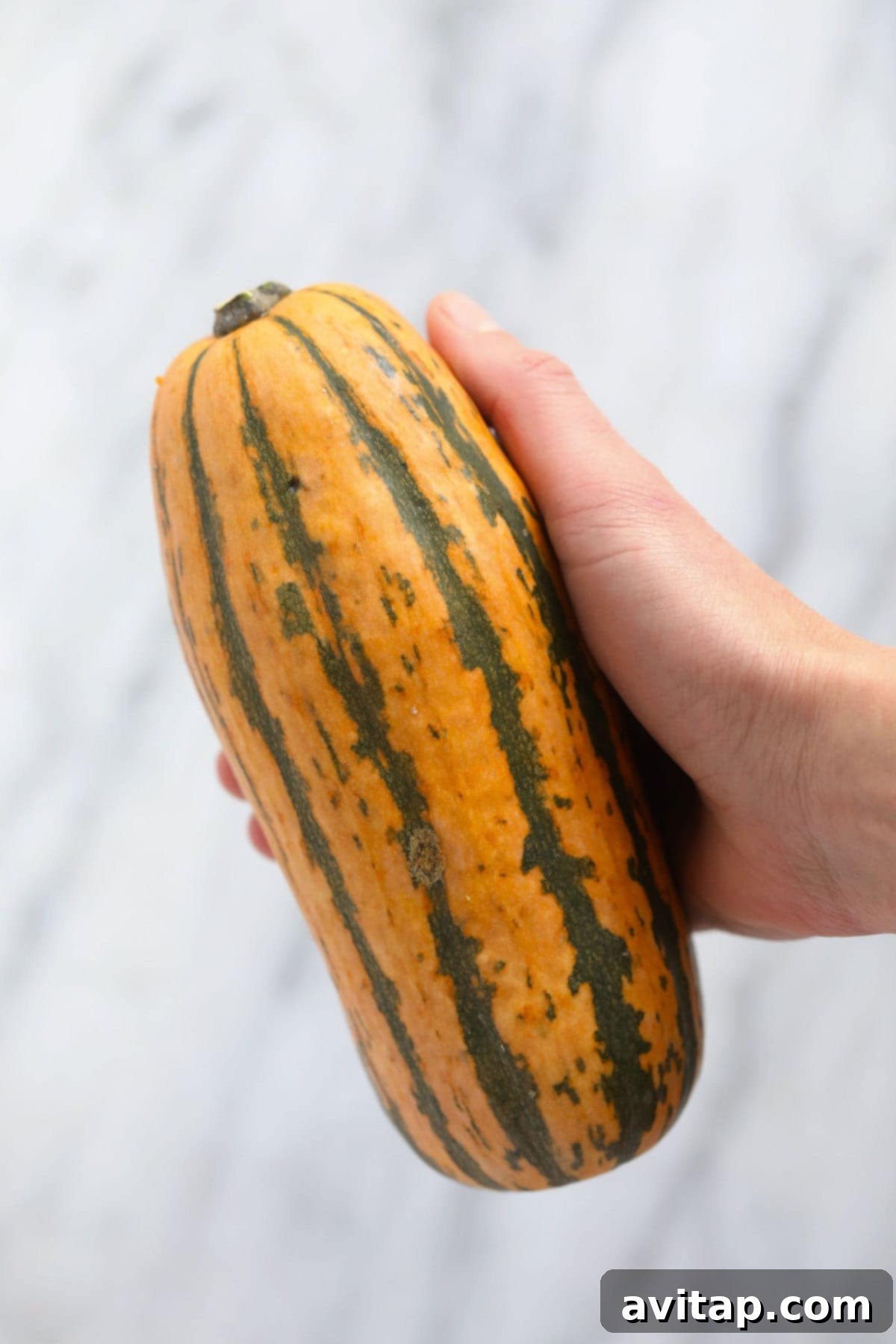 Two vibrant, whole delicata squashes resting on a rustic wooden board, ready for preparation.