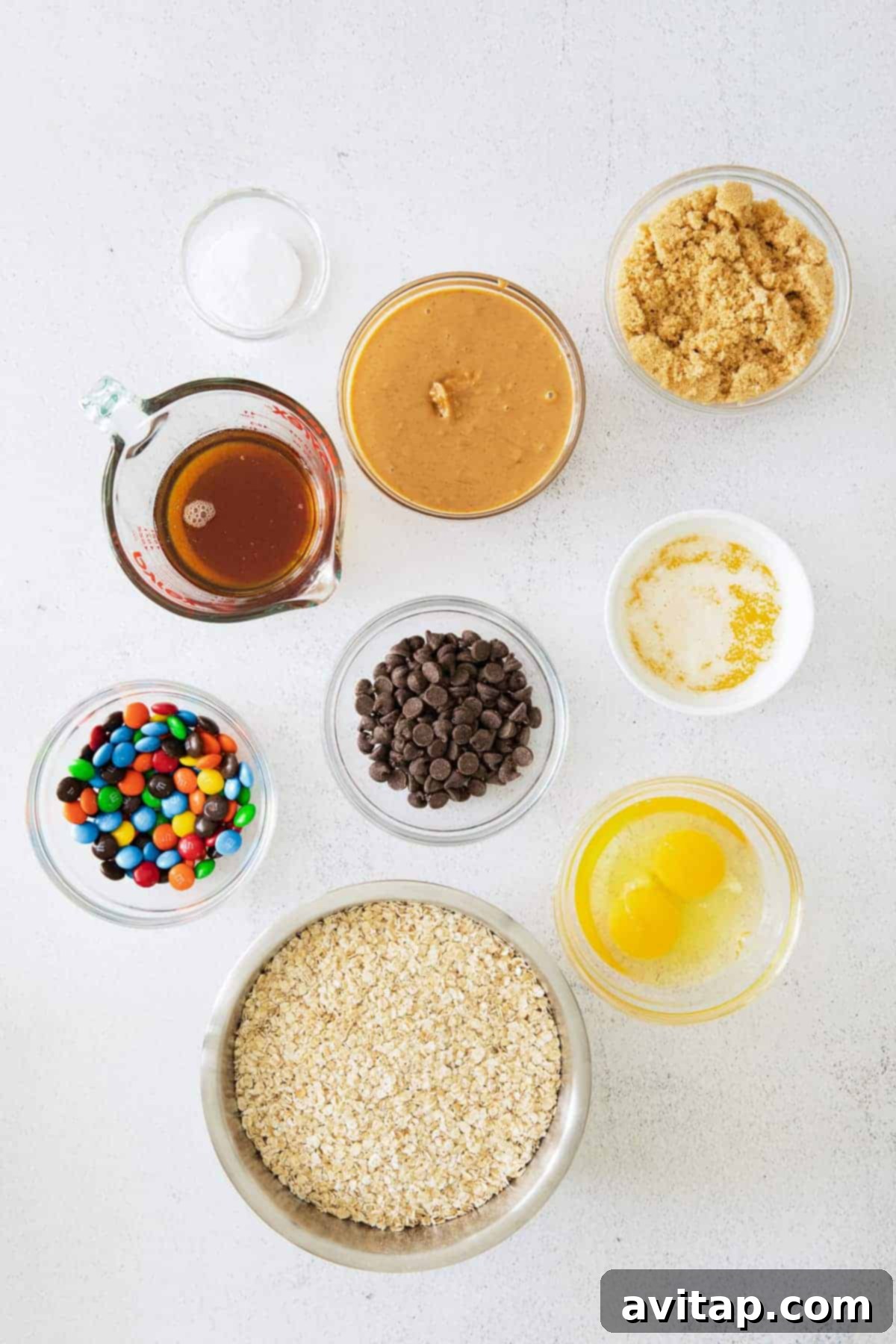 All ingredients for monster cookie bars laid out on a kitchen countertop, including oats, peanut butter, M&M's, and chocolate chips.