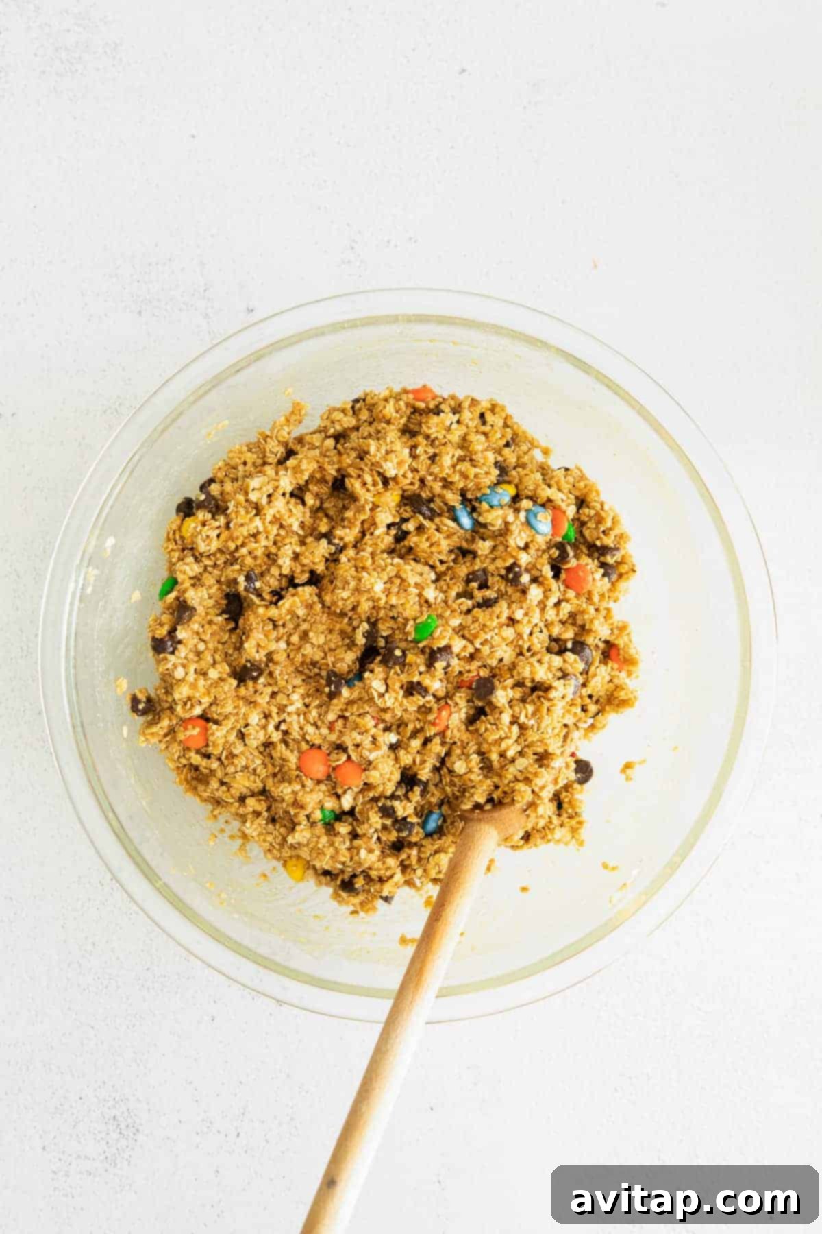 Thick, rich monster cookie bar dough with visible oats, M&M's, and chocolate chips in a large mixing bowl.