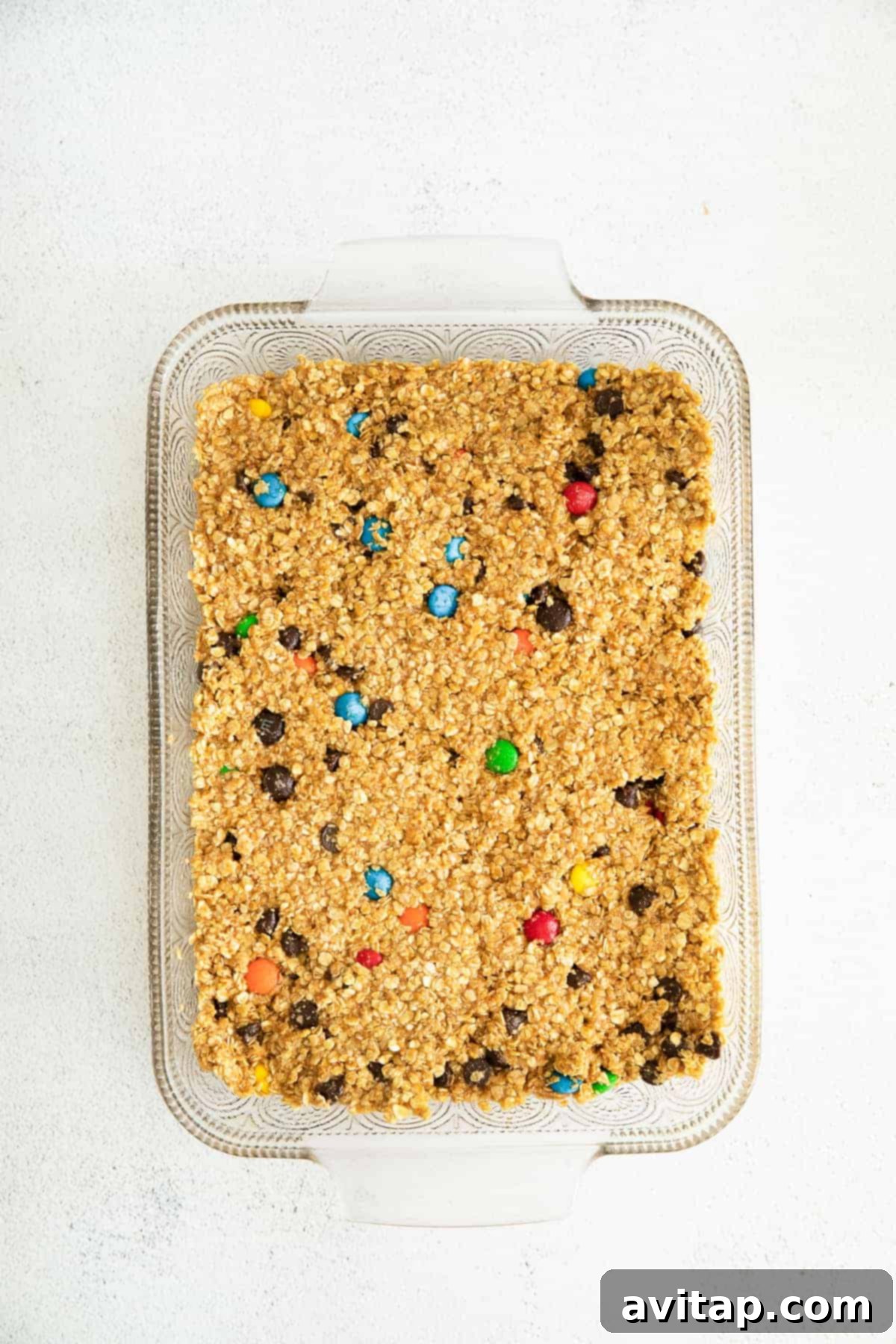 Monster cookie bar dough pressed firmly and evenly into a 9x13-inch baking dish, ready for baking.