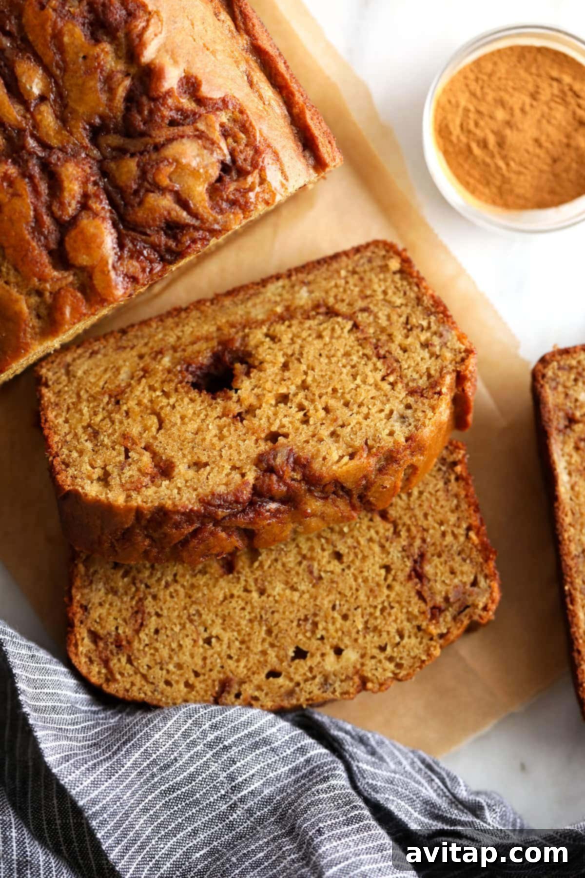 A generous slice of cinnamon swirl banana bread on a rustic cutting board, showcasing its beautiful, rich brown swirl.