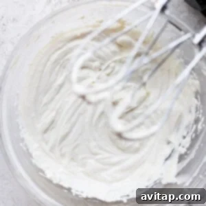 Cream cheese frosting in a bowl being whipped by a hand mixer.