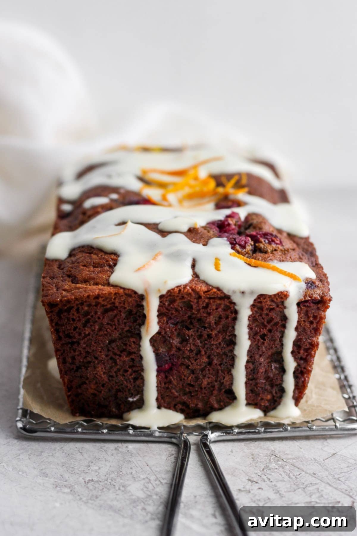 A freshly baked cranberry orange bread loaf generously covered with cream cheese glaze.