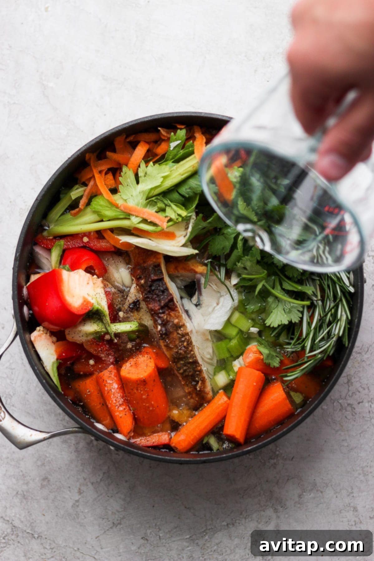 Pouring fresh water into a pot filled with chicken bones, an array of colorful vegetables, and aromatic herbs.