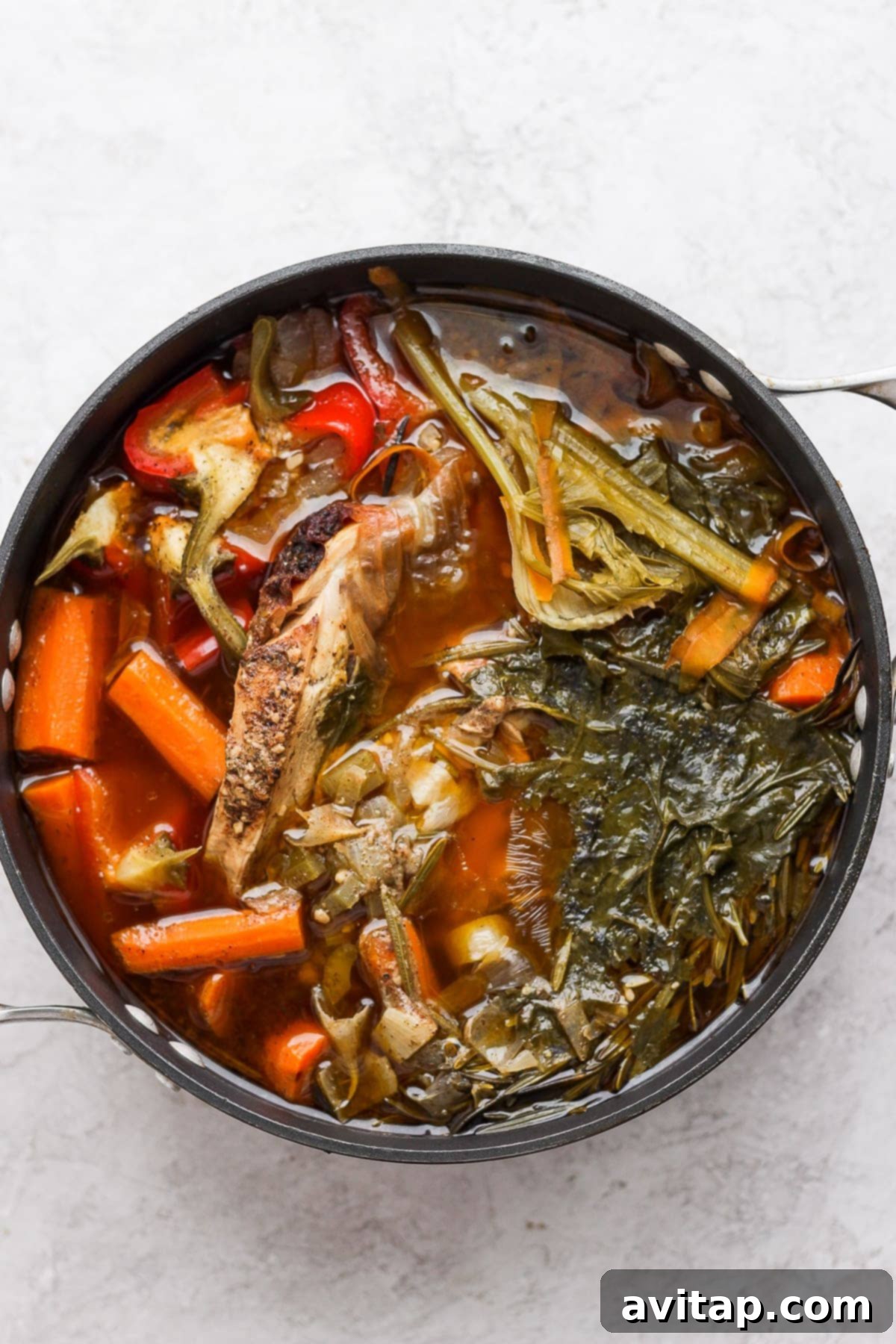 A pot of rich, golden chicken broth after simmering all day, filled with tender vegetables and chicken pieces.