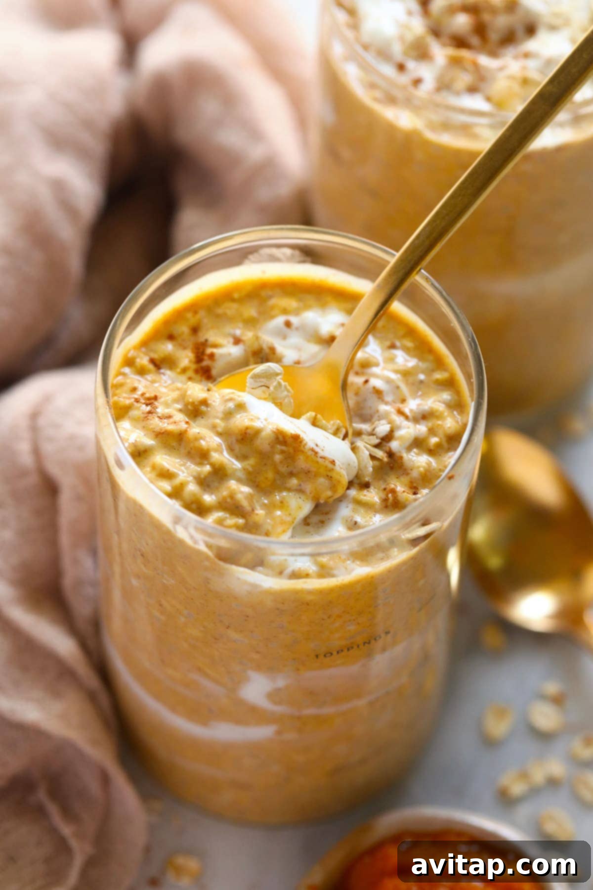 Ready-to-Eat Pumpkin Overnight Oats A spoon diving into a jar of creamy pumpkin cheesecake overnight oats, topped with autumn spices.