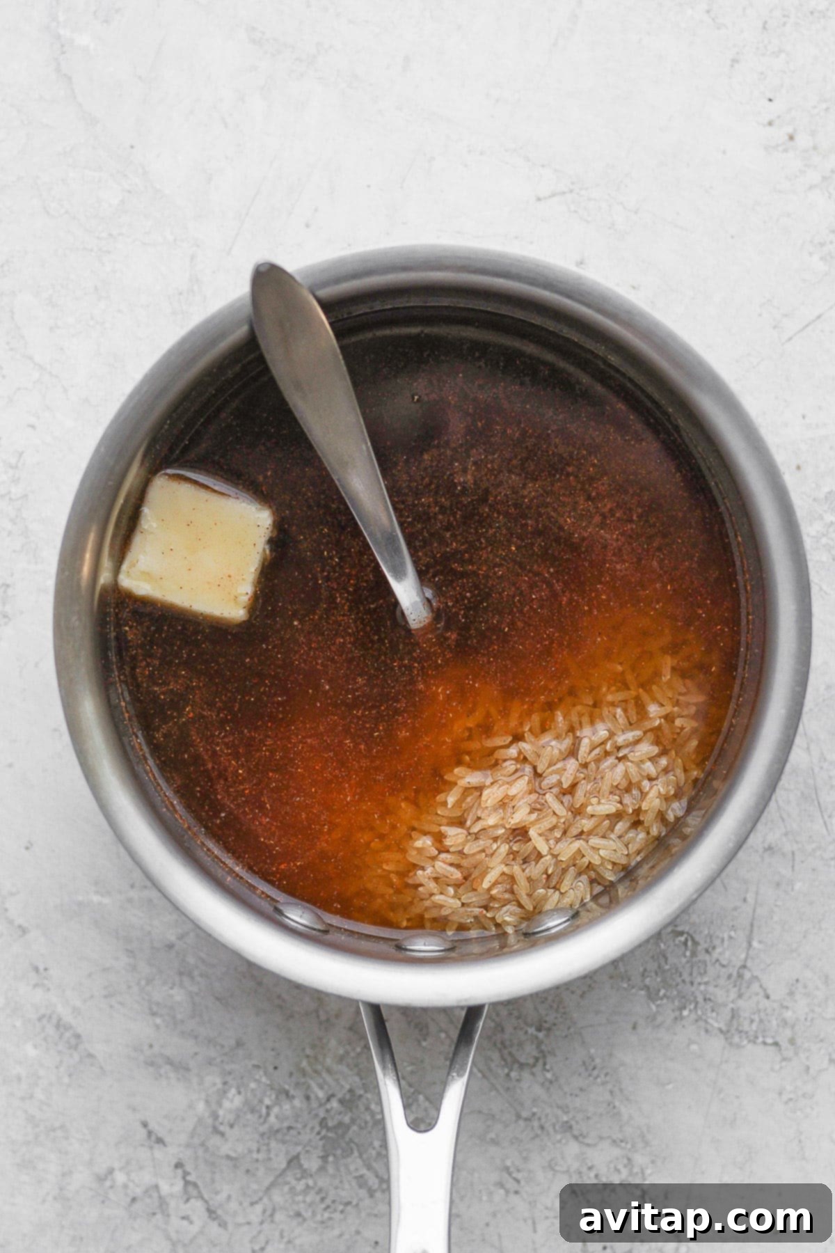 Uncooked brown rice and rich beef broth, essential components for the flavorful base of our red beans and rice, ready to be cooked in a stock pot.