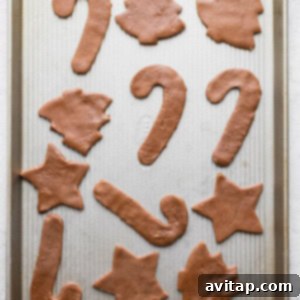 Various Christmas-themed cookie shapes, made from gingerbread dough, arranged on a baking sheet.