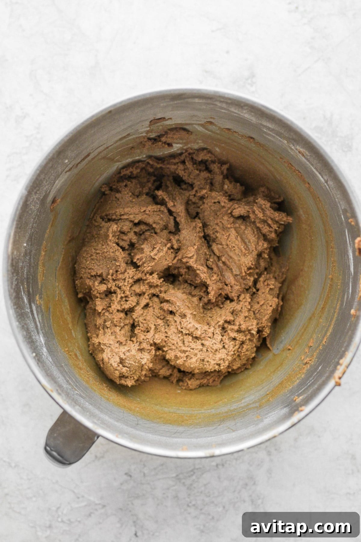 Gingerbread cookie dough expertly mixed in a stand mixer bowl, showcasing its rich, warm brown color.