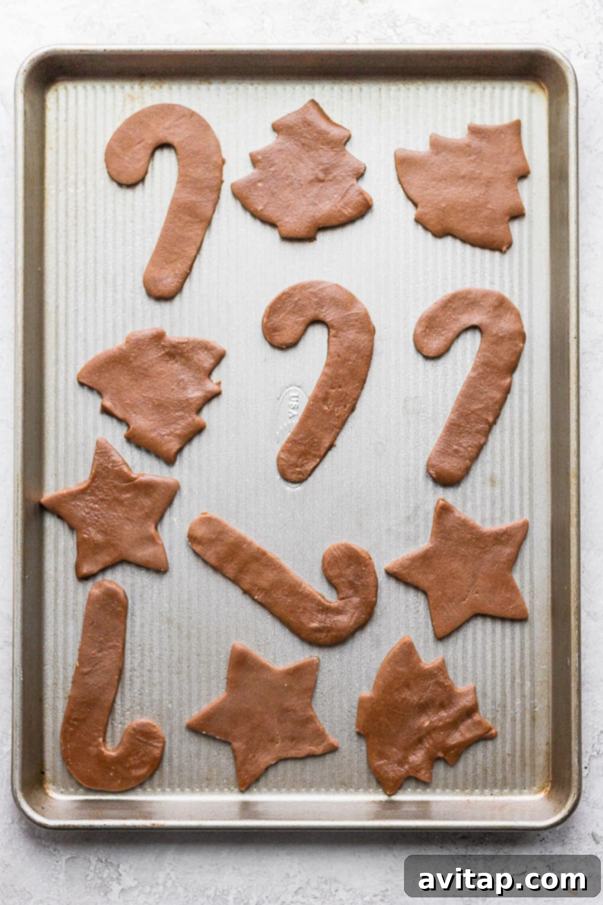 Raw gingerbread cookie dough cut into festive shapes arranged on a parchment-lined baking sheet, ready for the oven.