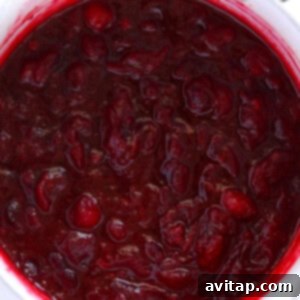Cranberry sauce simmering in a pot on the stovetop, thickening nicely.
