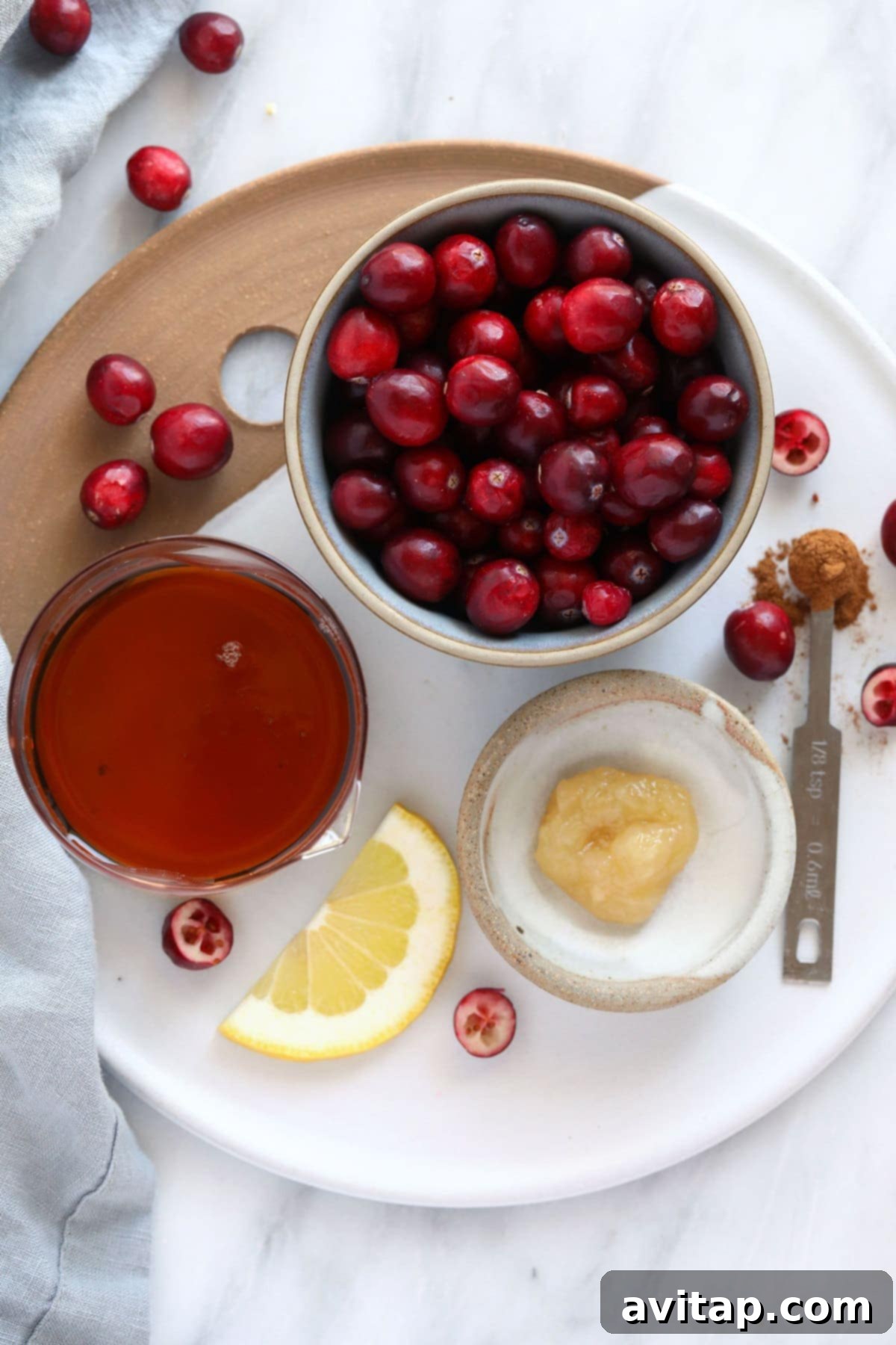 Fresh ingredients laid out for homemade lemon ginger cranberry sauce, including whole cranberries, lemon, ginger, and maple syrup.