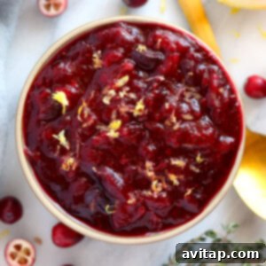 Unique cranberry sauce recipe served in a bowl with lemon slices and thyme for garnish.