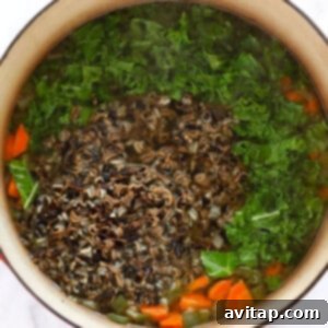A chicken and wild rice soup with carrots and greens in it.