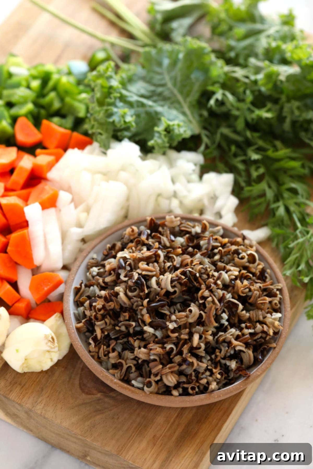 A vibrant selection of fresh ingredients including carrots, onions, kale, and wild rice, neatly arranged and ready for cooking a delicious soup.