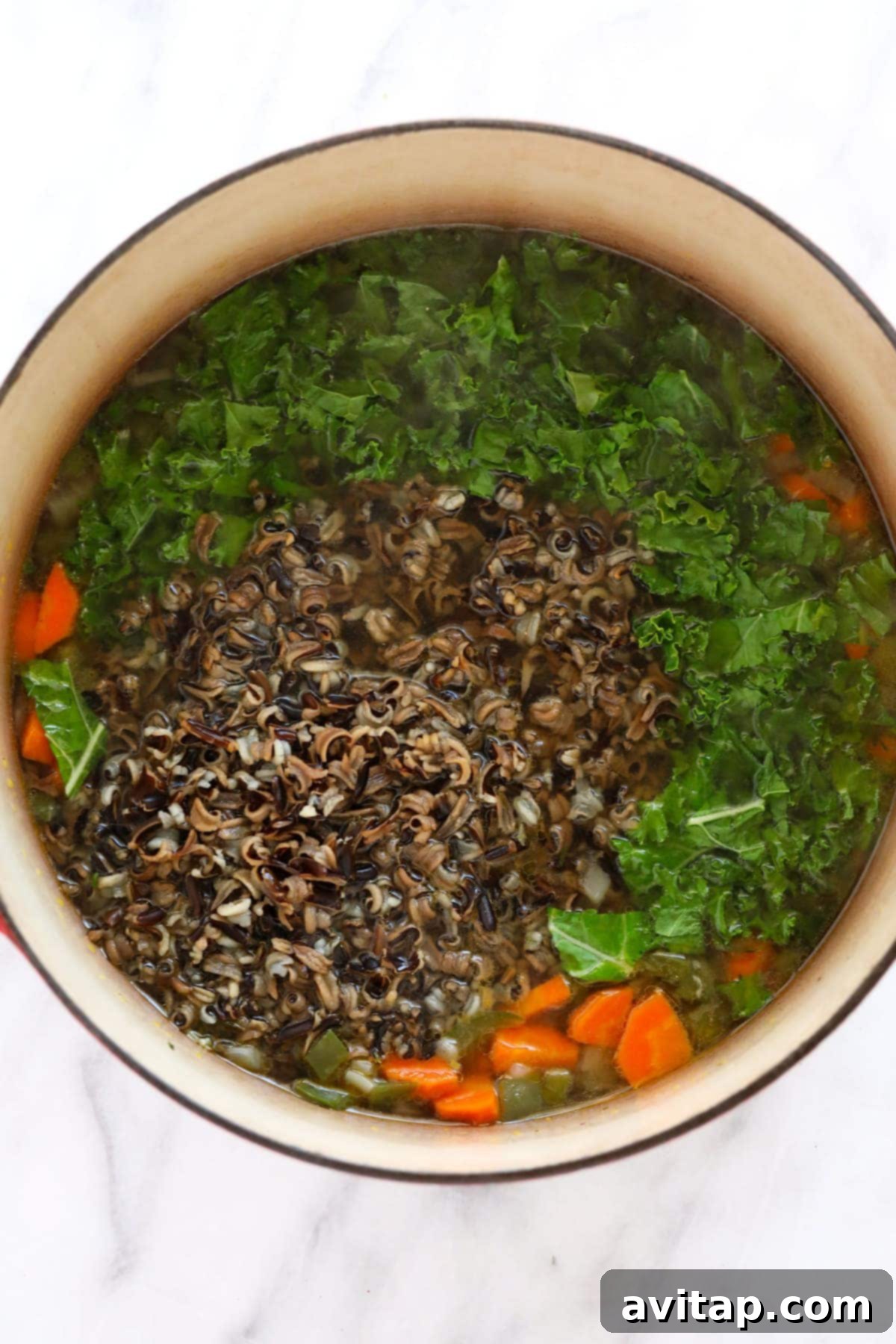 Fresh chicken breasts, colorful vegetables, and wild rice submerged in a savory chicken broth within a large stock pot, ready to simmer.