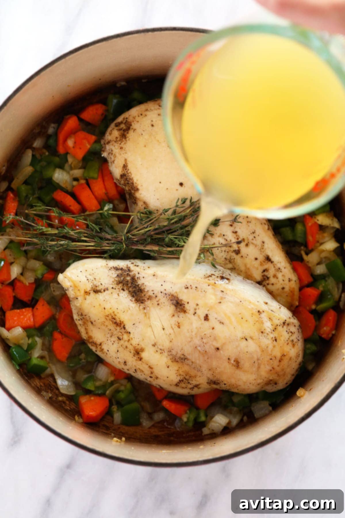 Broth being poured over chicken breasts and other ingredients for chicken wild rice soup, ready to simmer. Searing chicken breasts and vegetables in a stockpot before adding broth for chicken wild rice soup.