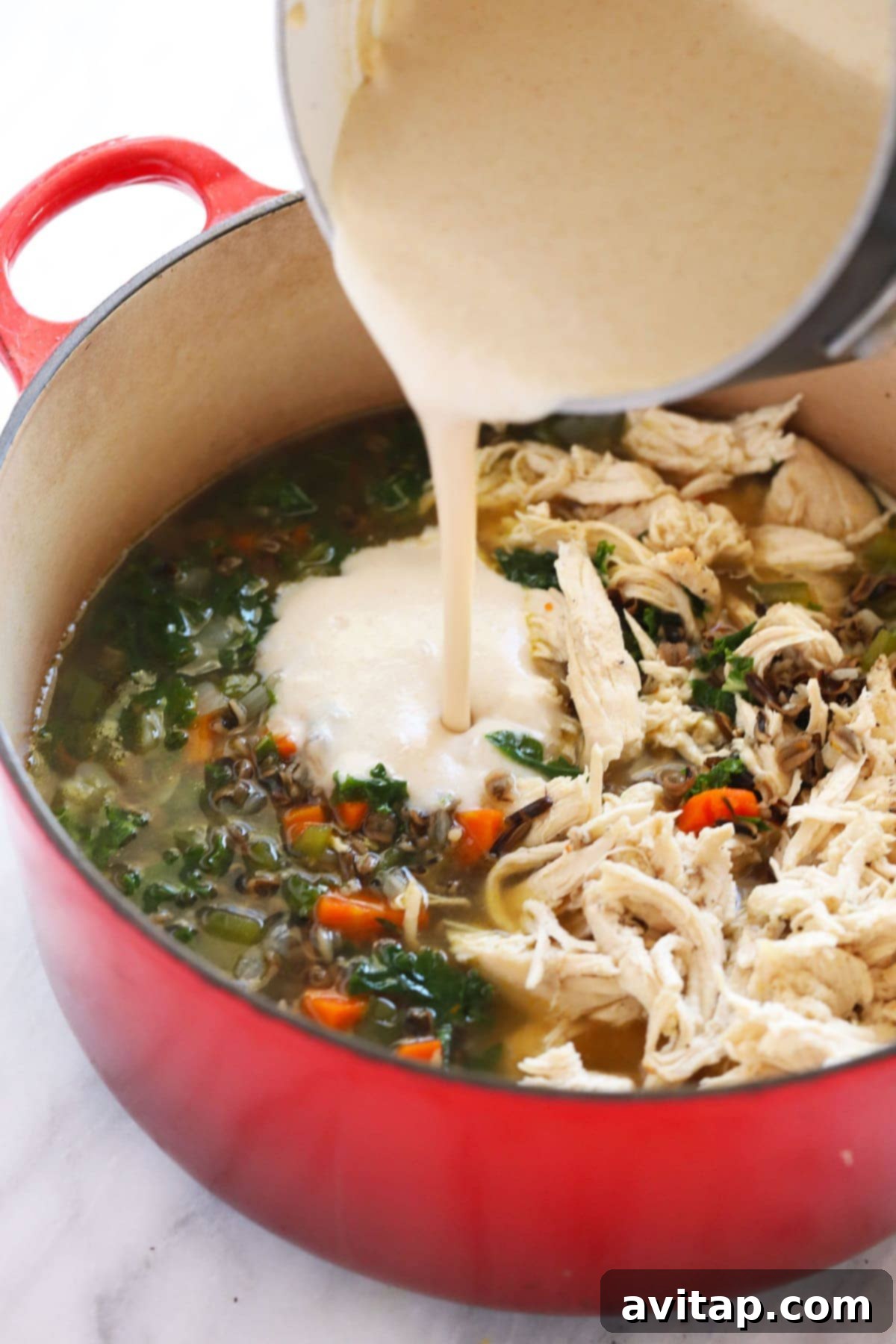 A rich, creamy roux being carefully poured into a simmering pot of chicken wild rice soup, transforming its texture.