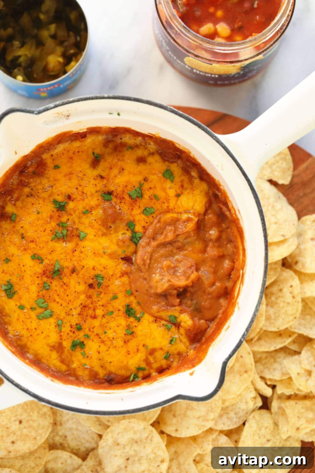 Irresistible baked bean dip in a cast iron skillet, generously covered in bubbly, golden melted cheddar cheese, ready to be served with tortilla chips.