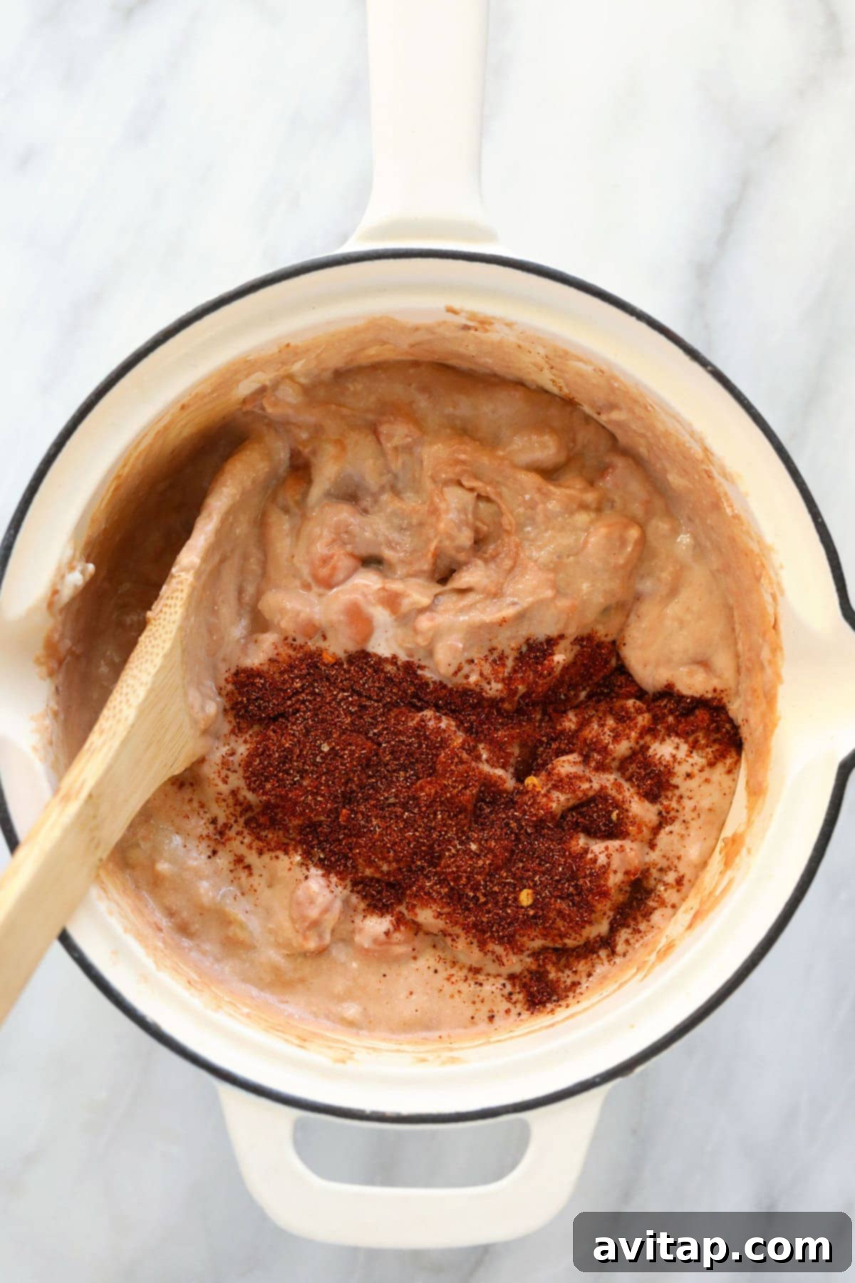 Close-up of bean dip ingredients being expertly mixed together in a large skillet on the stovetop with a spatula, creating a smooth, cohesive mixture.