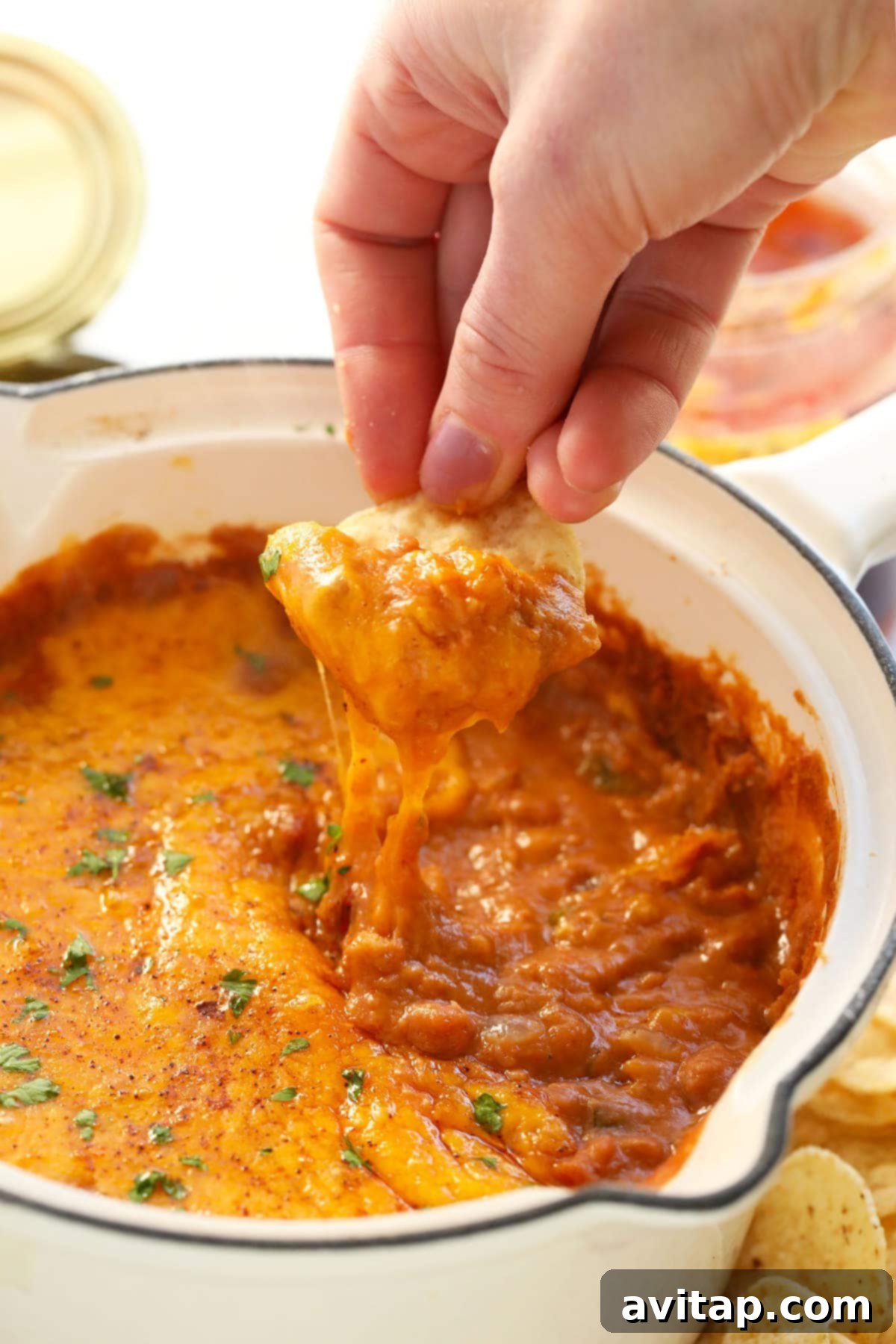 Perfect scoop of cheesy bean dip on a crispy tortilla chip, showcasing the rich, melted cheddar cheese and hearty bean mixture, ready to be eaten.