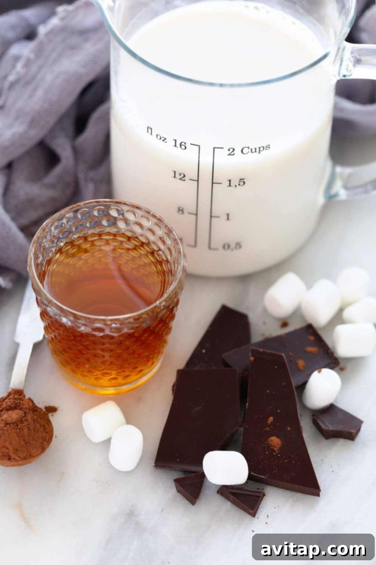 Ingredients for spiked hot chocolate laid out on a surface, including milk, dark chocolate, cocoa powder, maple syrup, and bourbon.