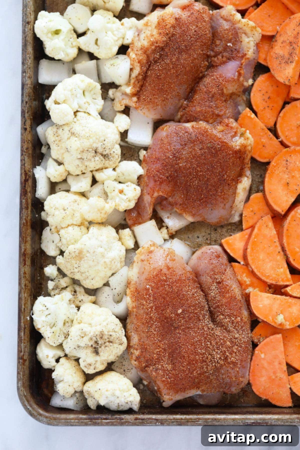 Perfectly seasoned chicken thighs, chunky sweet potatoes, roasted cauliflower florets, and sliced onions baking together on a single sheet pan, creating a vibrant and aromatic dinner.