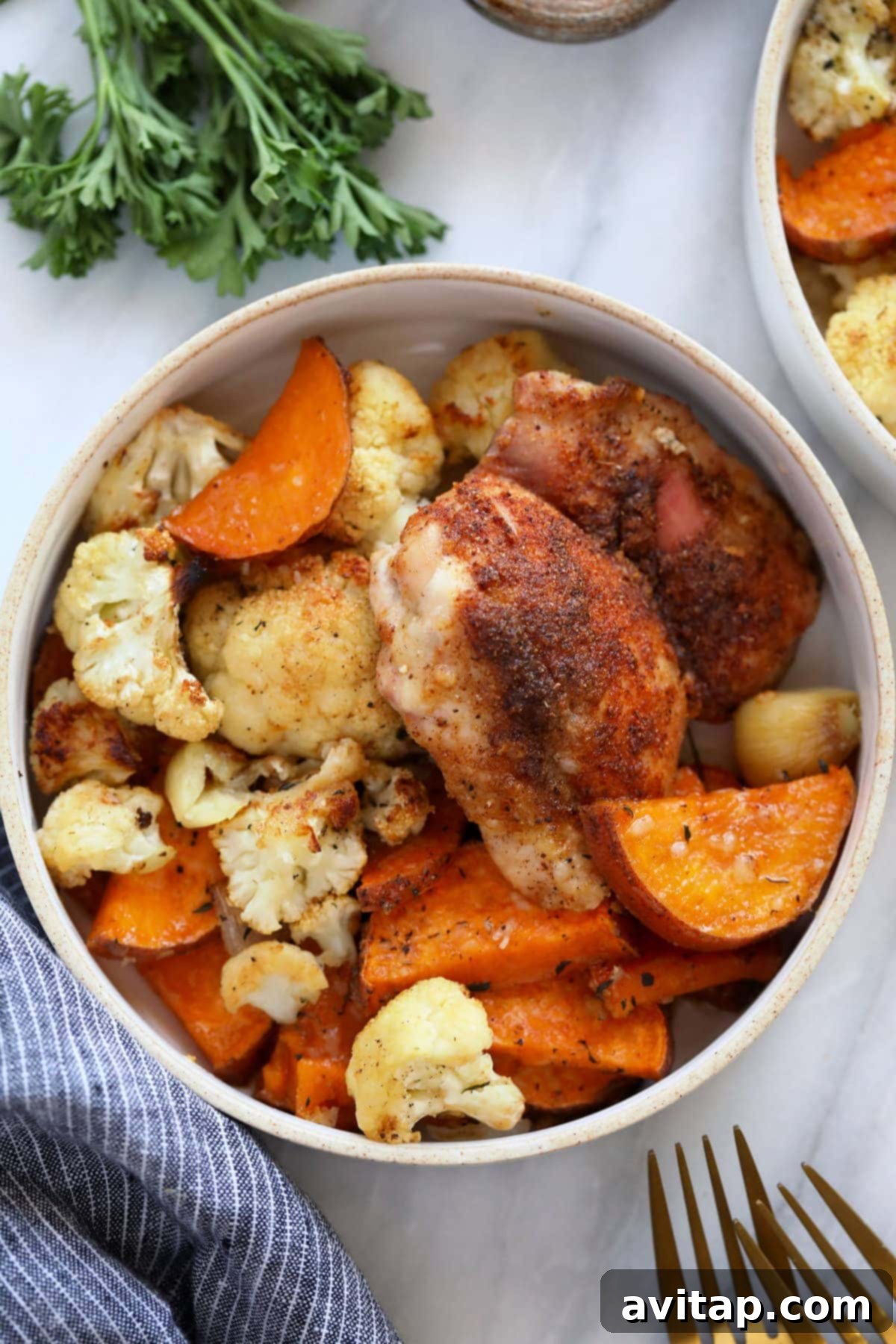 A vibrant bowl filled with perfectly roasted chicken thighs, tender cauliflower, and sweet potato chunks, ready to be customized with additional grains or greens.