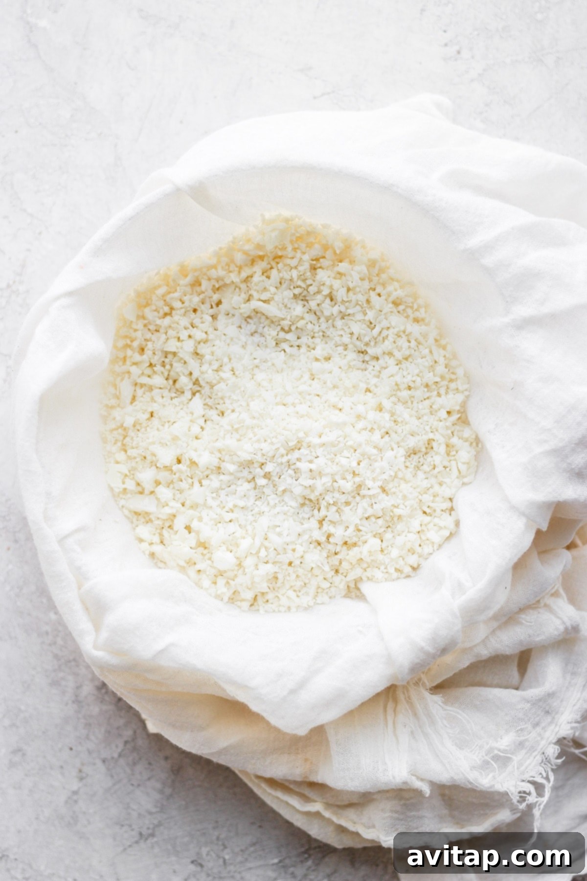 Finely processed cauliflower rice resting in a tea towel, ready for moisture extraction.