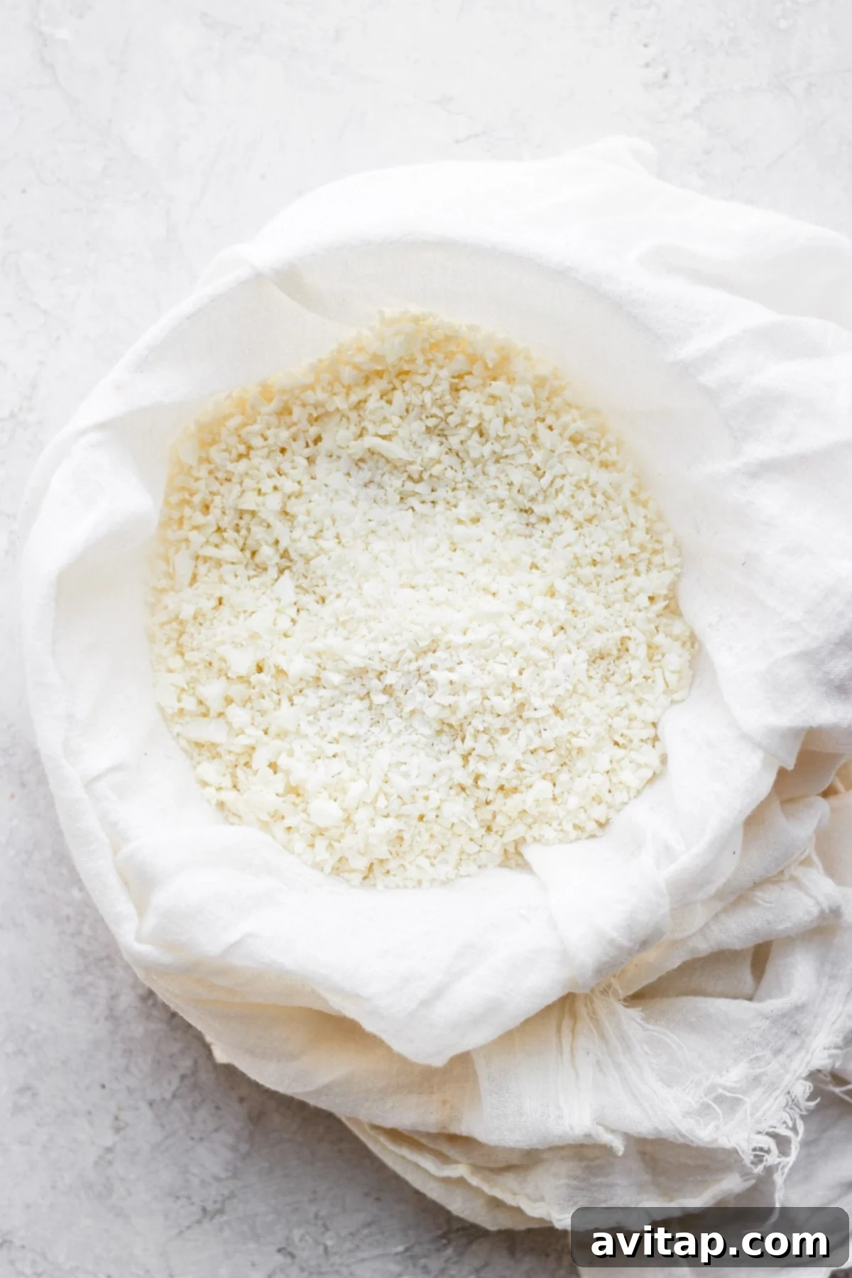 Veggie Powered Pizza Crust 4 Finely processed cauliflower rice expertly wrapped and squeezed in a clean tea towel, illustrating the moisture removal step for the pizza crust.