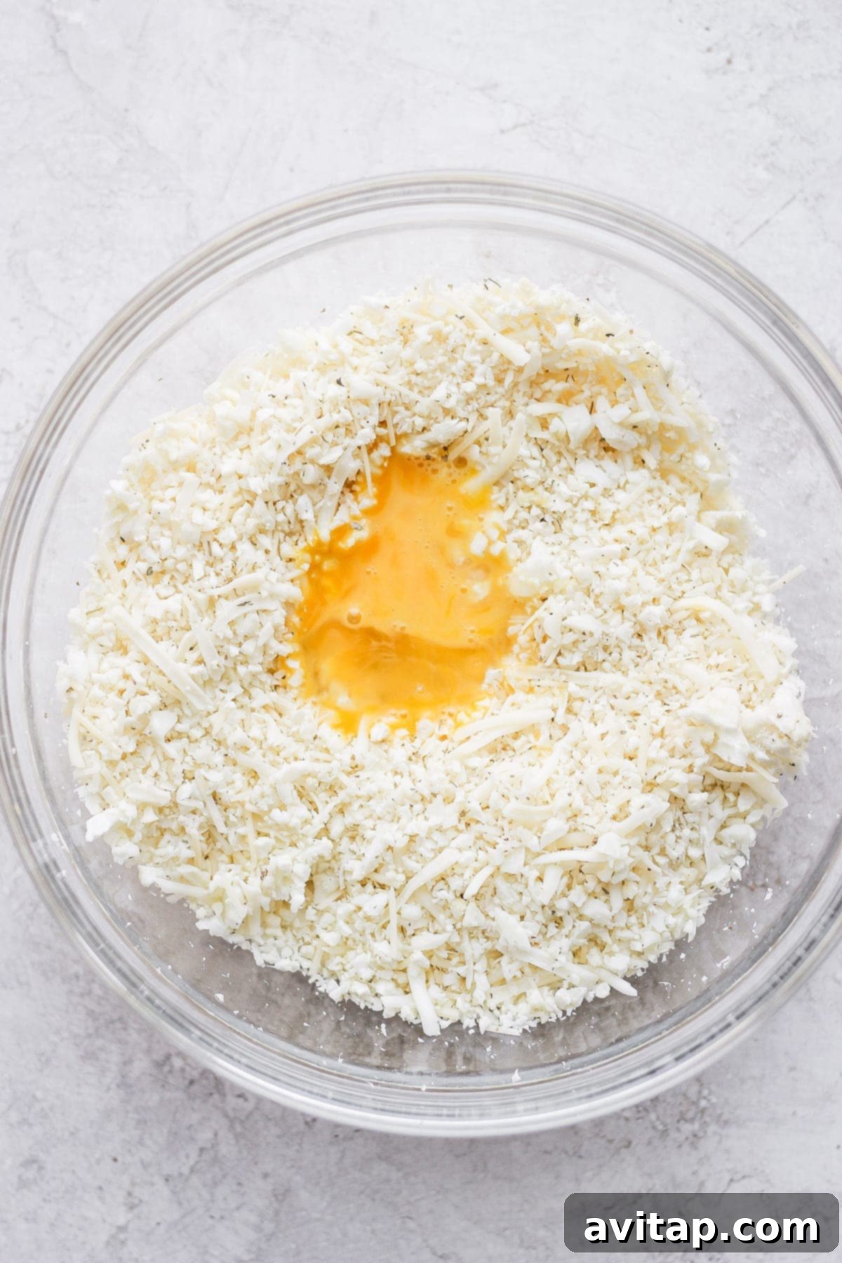 Veggie Powered Pizza Crust 5 A large bowl containing finely processed cauliflower rice, shredded cheeses, and a whisked egg, ready to be mixed into a pizza crust dough.