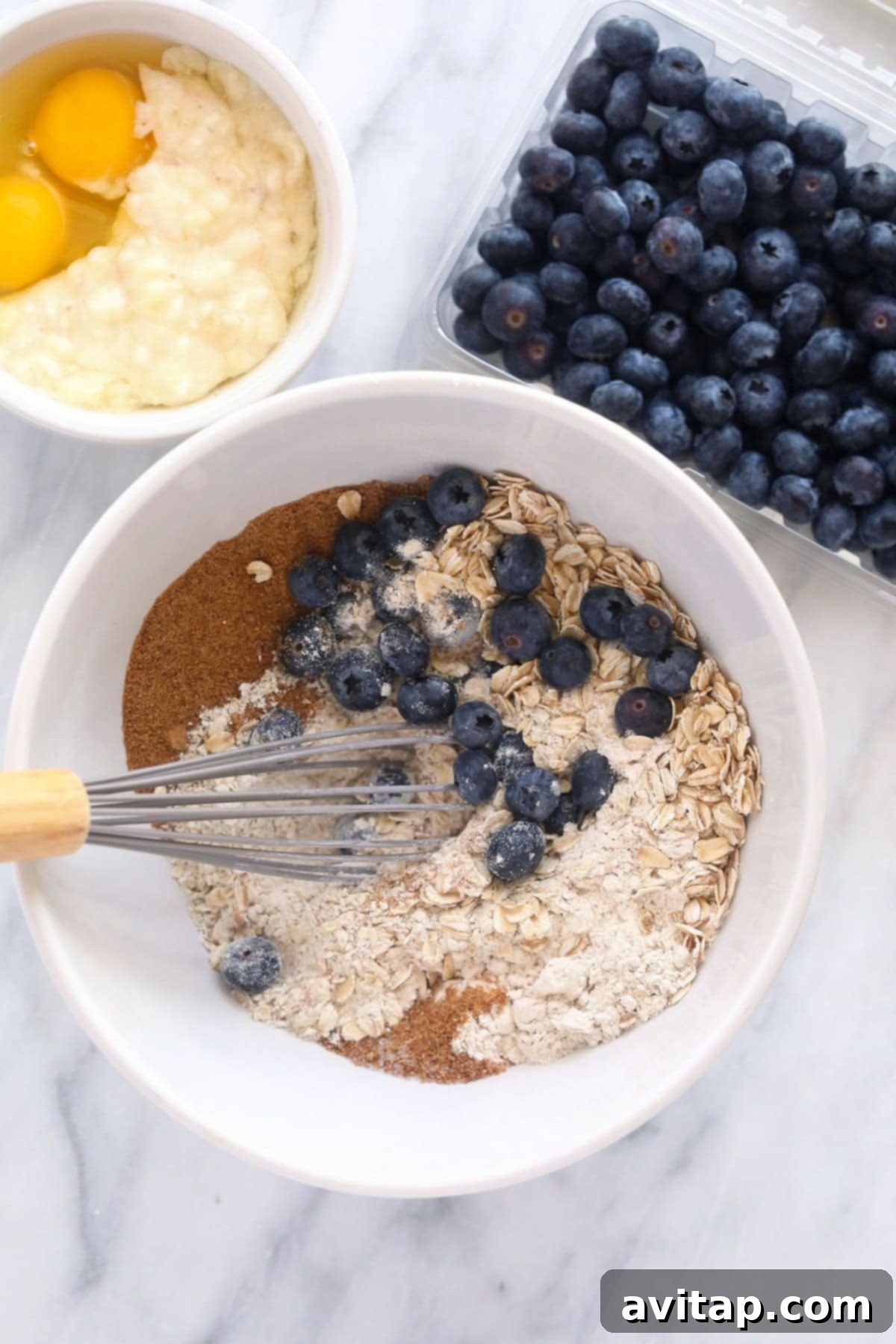 A vibrant assortment of fresh ingredients for blueberry oatmeal muffins, including flours, oats, eggs, and ripe blueberries, neatly arranged in a bowl, ready for mixing.