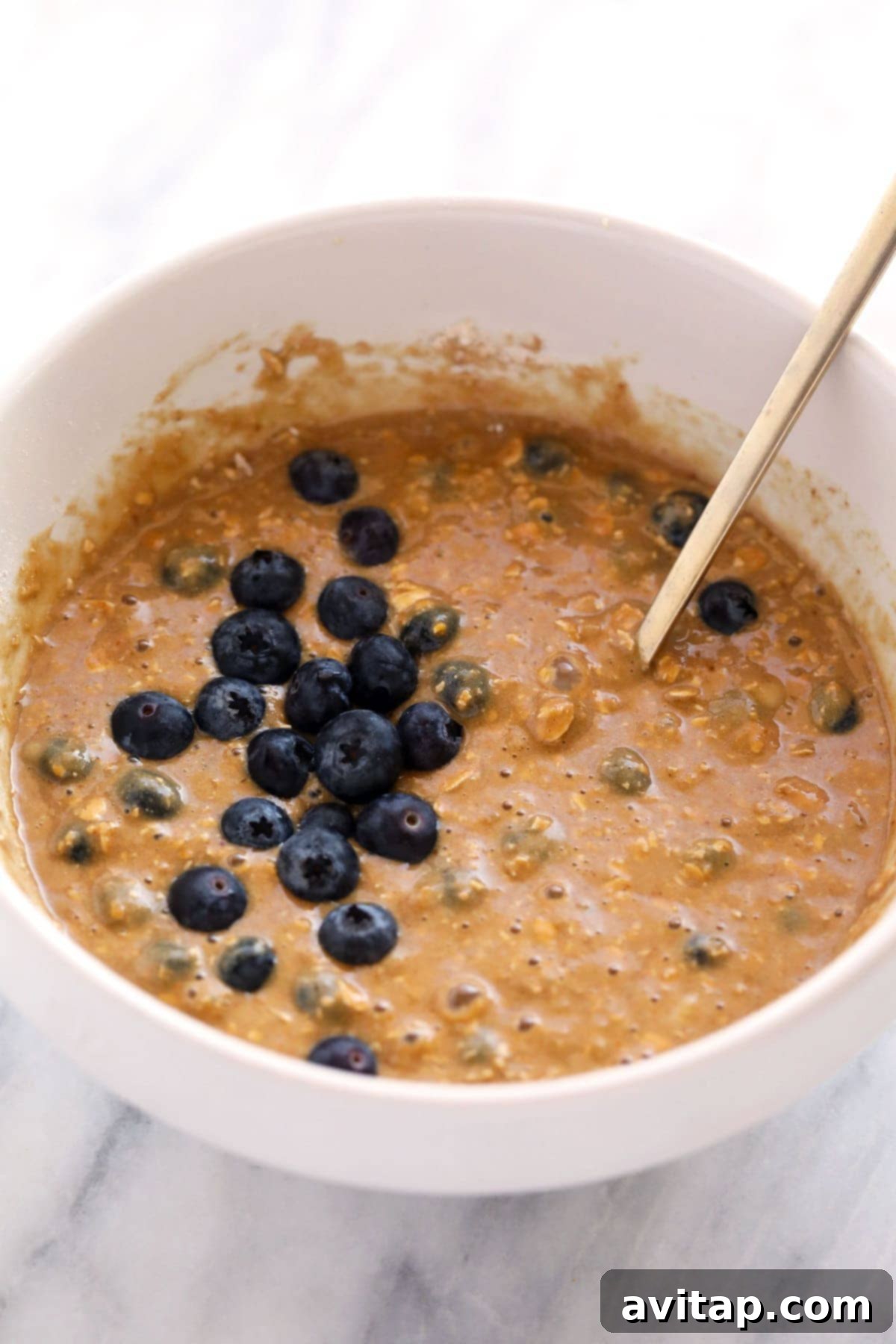 Thick, vibrant blueberry oatmeal muffin batter glistening in a mixing bowl, ready for the muffin tin.