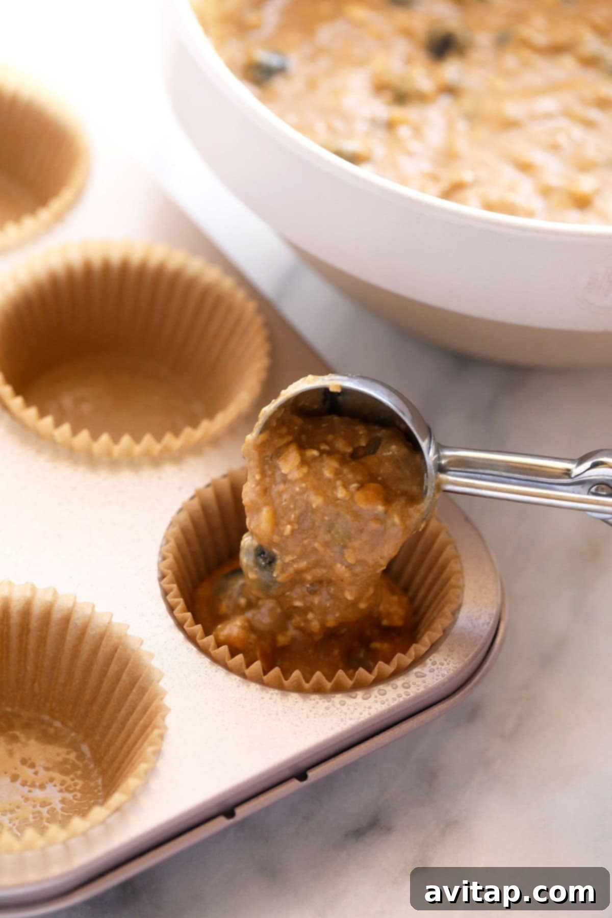 Blueberry muffin batter being carefully poured into paper liners within a muffin tin, ready for baking.