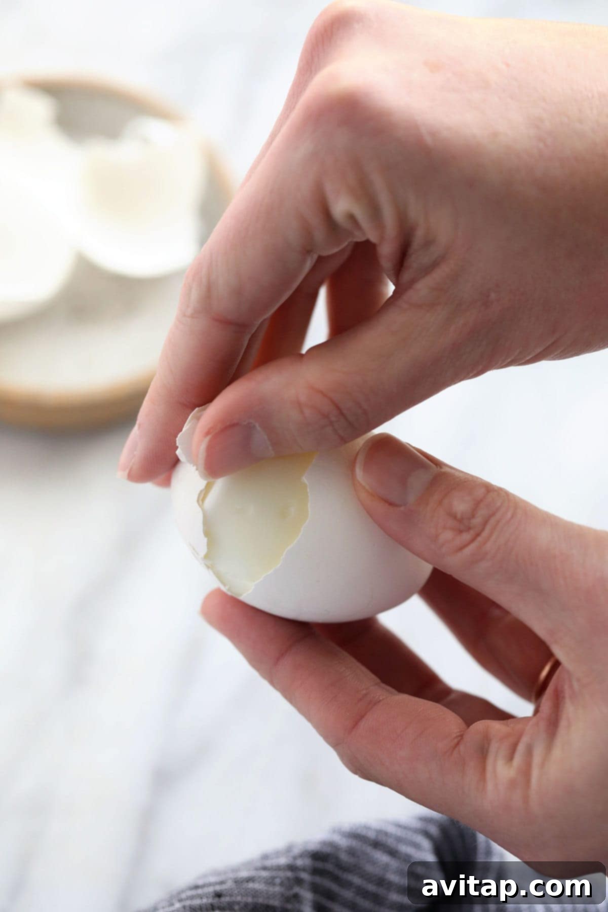 A hand gently peeling the shell from a perfectly cooked hard boiled egg.