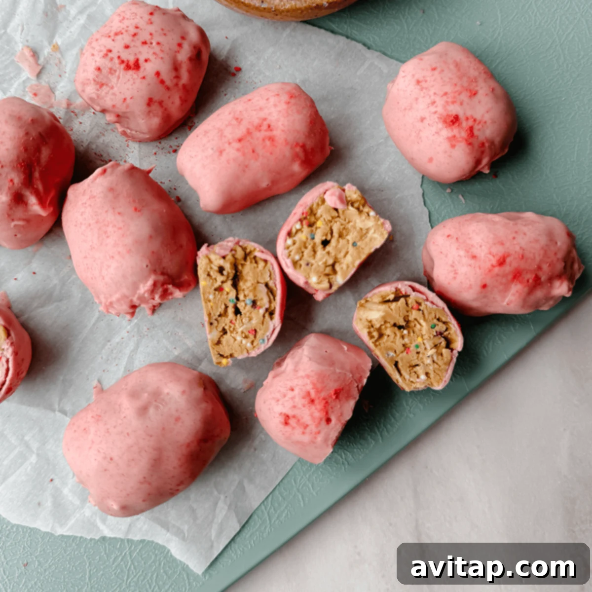 Pink-coated truffles arranged on parchment paper, with some sliced open to reveal a delightful cake-batter-like filling adorned with colorful sprinkles.