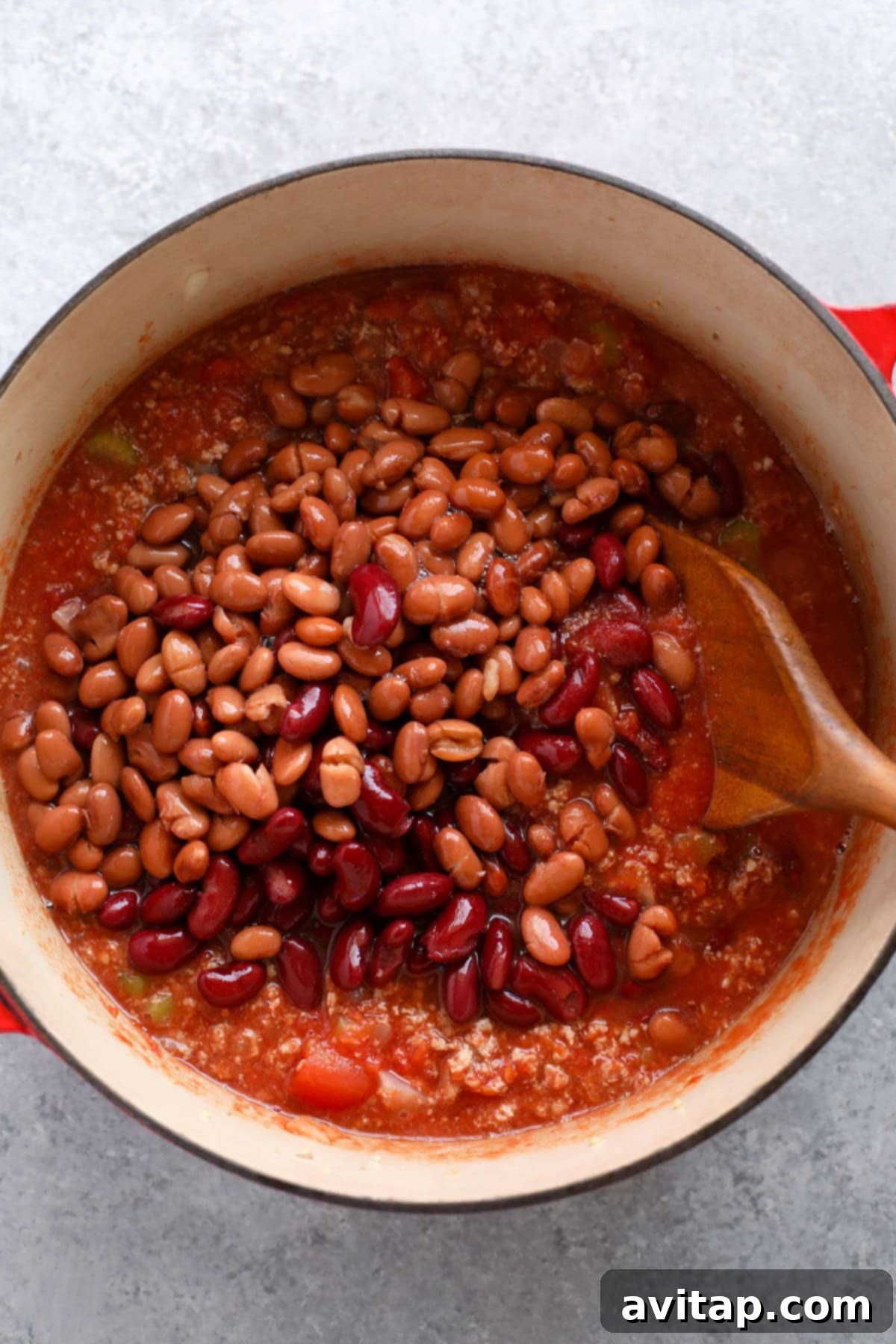 Adding Beans to Turkey Chili for a Hearty and Wholesome Meal Canned pinto and red kidney beans being added to a large pot of simmering turkey chili, enriching its texture and flavor.