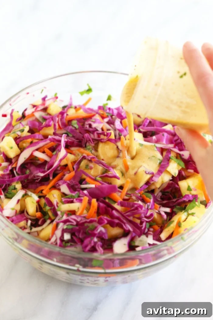 Hand pouring tangy dressing over a bowl of colorful coleslaw ingredients