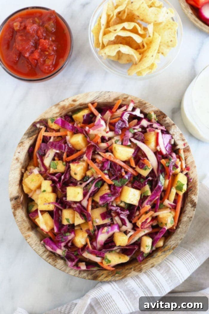 Pineapple coleslaw in a serving bowl with other BBQ side dishes like corn and grilled vegetables